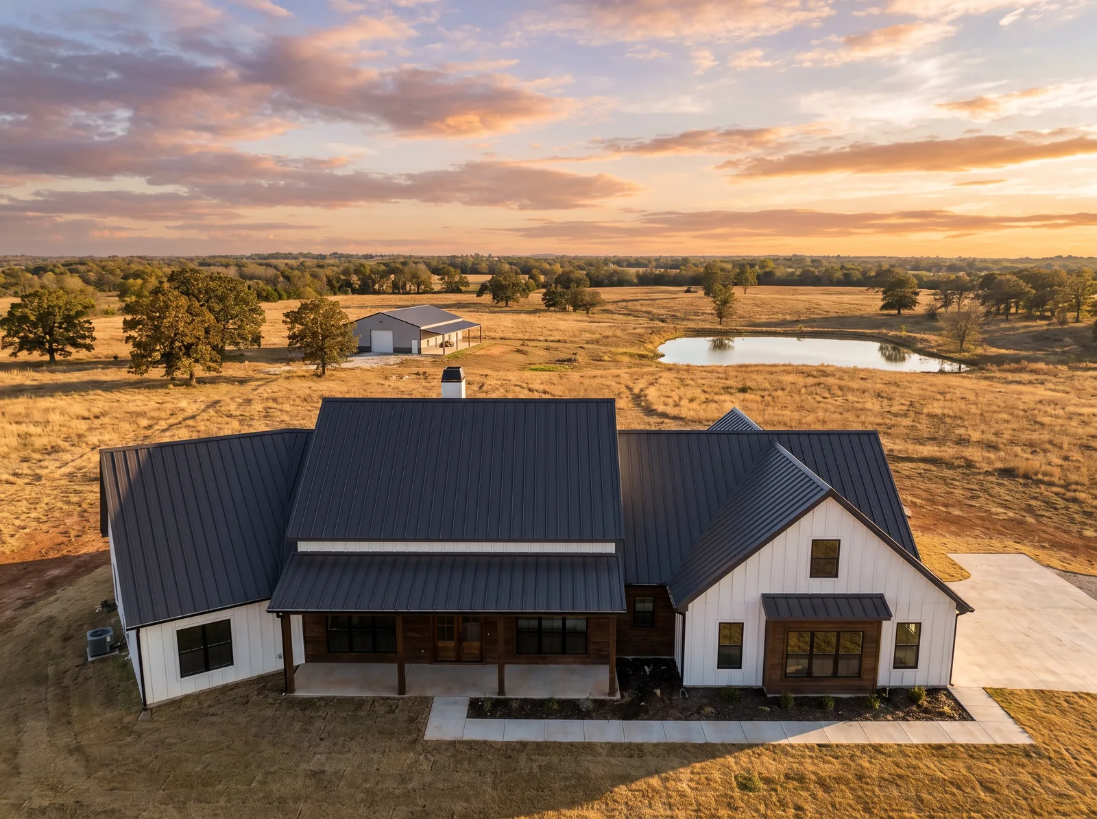 New charcoal standing-seam metal roof on a farmhouse-style home on an acreage lot east of Broken Arrow with a pond and open pasture behind